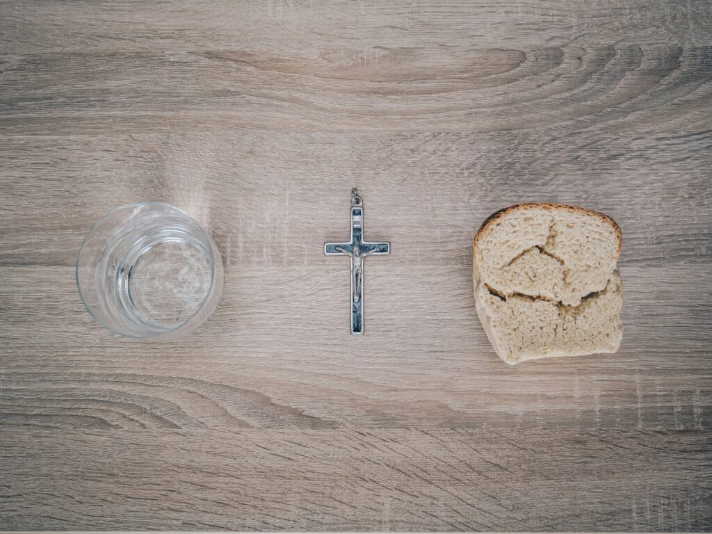 Ein Glas Wassre, ein Kreuz und ein Stück Brot auf einem Holztisch während der Fastenzeit